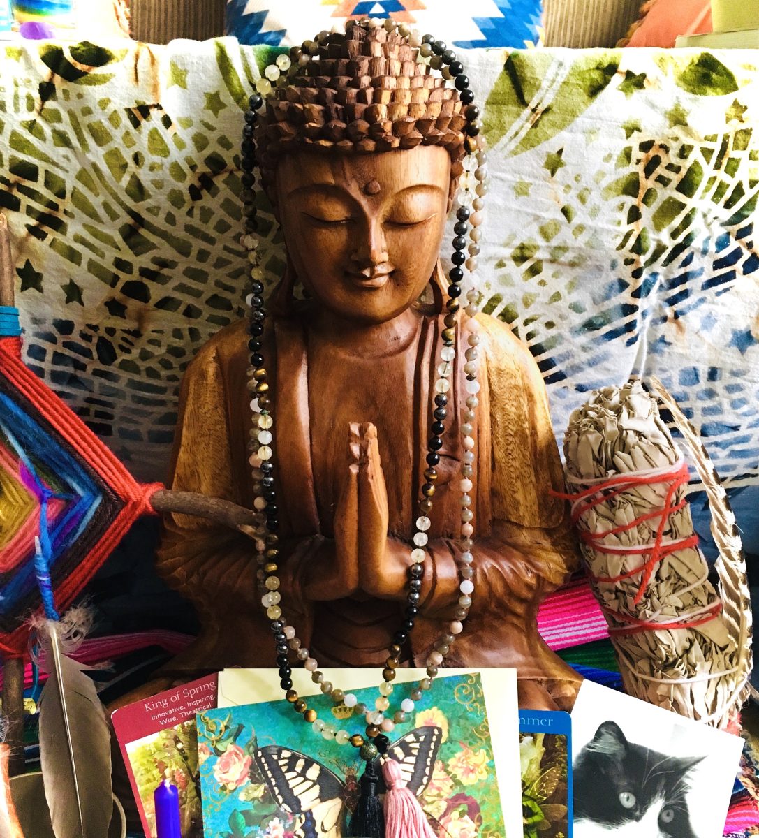 Wooden Buddha statue with prayer beads, meditation altar items, sage bundle, and spiritual cards — symbolizing Buddhism, Buddhist mindfulness, meditation, Reiki Master energy healing, Reiki sessions, and personal growth through being present.